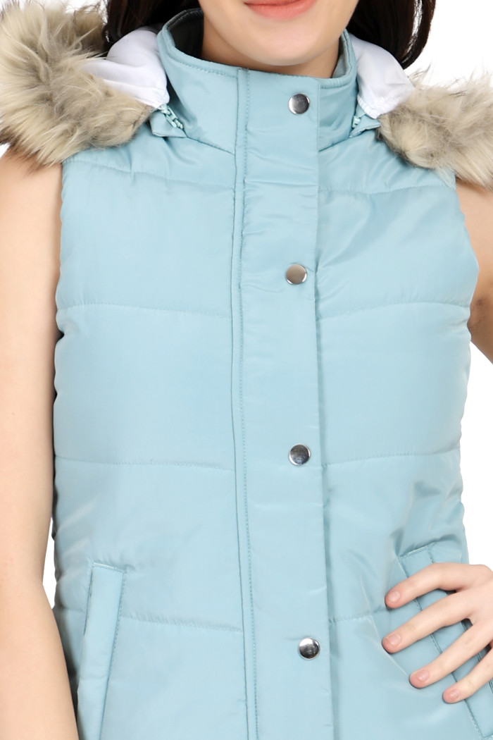 A cropped image of a woman wearing Trufit’s sea green half-sleeve quilted jacket with button placket, zip closure, side pockets, and a removable hood with her left hand on her waist.